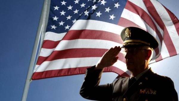 Silhouette of veteran US Army Colonel Chaplain wearing hat and saluting with an American flag flying behind him.