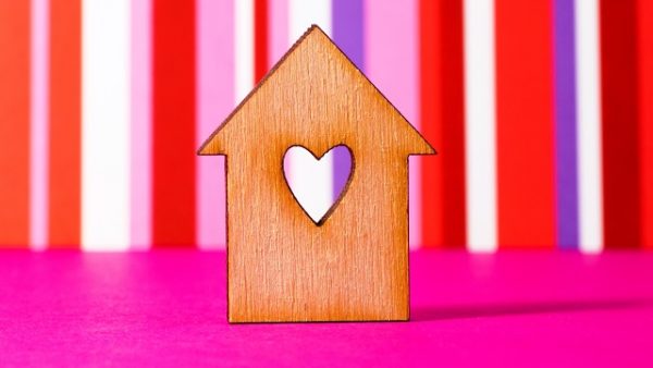 Wooden house with hole in the form of heart on red striped background